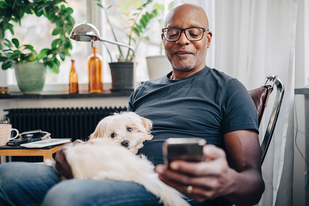 Older man looking at phone with dog in lap